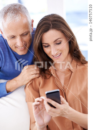 Couple, smartphone and smile on sofa to relax with reading, search and mobile app for contact with bonding. People, woman and mature man with phone for notification, typing or web connection in house 140757510