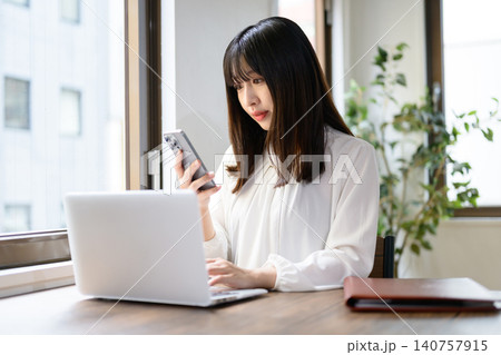 オフィスでノートパソコンとスマホを使って仕事をする日本人女性 140757915