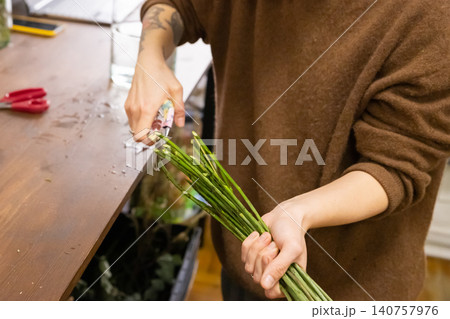 Florist woman pruning green flower stems with garden shears. Professional small business owner preparing bouquet in flower shop. Floral workshop and flower care preparation concept. 140757976