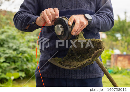 Man changes trimmer line for a string trimmer. Gardener does maintenance for gardening tool. Lawn care and yard work concept. Man changes trimmer line for a string trimmer. Gardener does maintenance for gardening tool. Lawn care and yard work concept. 140758011
