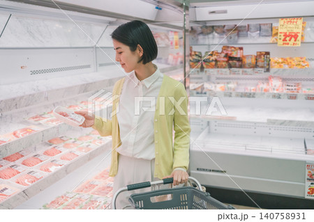 スーパーの精肉売り場でパック肉を手に取り品定めする女性客 140758931