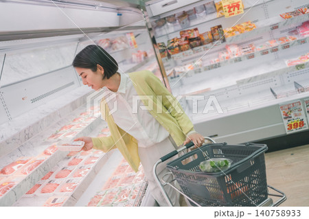 スーパーの精肉売り場でパック肉を手に取る女性客 140758933