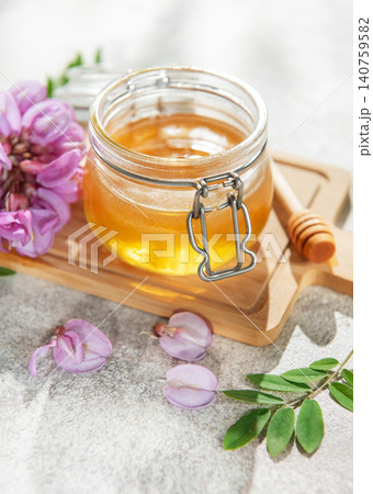 Acacia honey jar with blooming flowers and wooden dipper 140759582