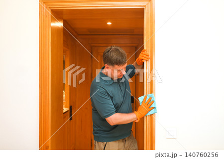 Adult father wiping dust from a door frame inside a tidy home during household cleaning routine Adult father wiping dust from a door frame inside a tidy home during household cleaning routine 140760256
