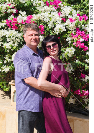 Adult couple embracing affectionately in front of blooming shrubs during a peaceful spring or summer moment Adult couple embracing affectionately in front of blooming shrubs during a peaceful spring or summer moment 140760261