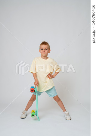 Distant full length view of a confident school-age boy posing with a mint skateboard standing vertically next to his leg. Clean minimalist white studio shot, perfect for space copy. Cute preteen boy Distant full length view of a confident school-age boy posing with a mint skateboard standing vertically next to his leg. Clean minimalist white studio shot, perfect for space copy. Cute preteen boy 140760416