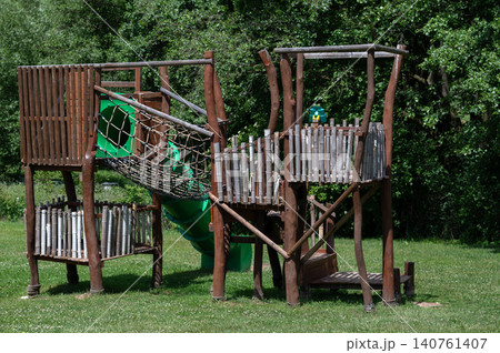 Wooden playground structure with slide and climbing net in grassy park setting Wooden playground structure with slide and climbing net in grassy park setting 140761407