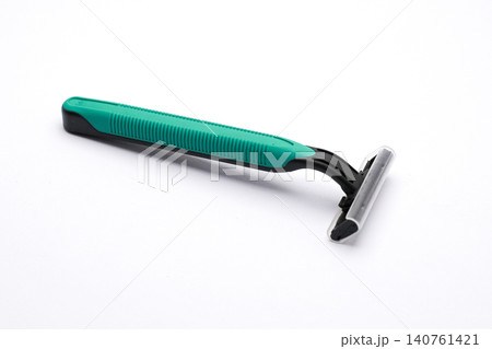 Green razor rests beside white tube on clean white surface. Minimalist setup highlights grooming essentials clearly. Ideal for beauty or personal care product advertisements 140761421