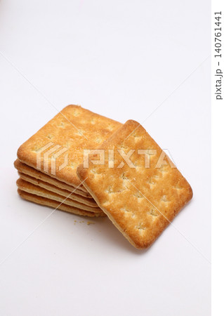 Golden crackers rest on plain white surface. Stacked neatly, one leans forward slightly. Crumbly texture shows crisp, baked perfection. Ideal for food, snack, or bakery promotional 140761441