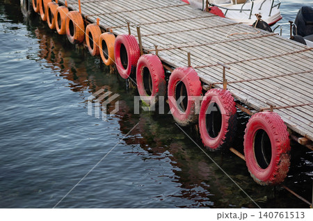 Wooden dock with colorful tires floating on water, reflecting sunlight in calm harbor 140761513