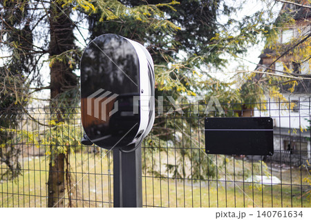 Electric vehicle charging station wallbox installed outdoors near house 140761634