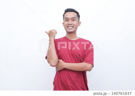 Young man smiles broadly, showing excitement. He gestures with both hands, pointing outward. He wears a plain red t-shirt. Background is clean white, uncluttered Young man smiles broadly, showing excitement. He gestures with both hands, pointing outward. He wears a plain red t-shirt. Background is clean white, uncluttered 140761837
