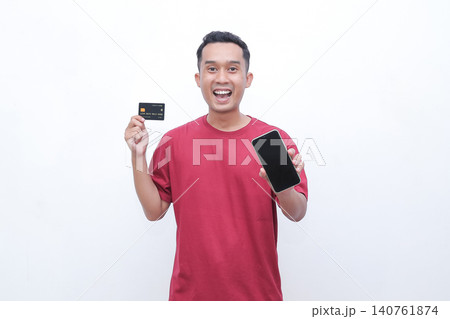 Man smiles brightly, holding card and phone. Simple white background, clean and focused. Ideal for payment or shopping concepts. Energetic expression suggests success or ease Man smiles brightly, holding card and phone. Simple white background, clean and focused. Ideal for payment or shopping concepts. Energetic expression suggests success or ease 140761874