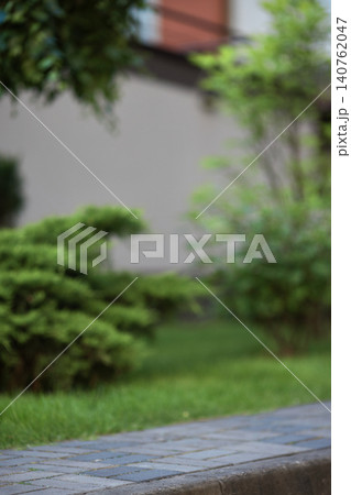Stone paver sidewalk bordering lush green grass and blurred foliage in a peaceful outdoor park scene Stone paver sidewalk bordering lush green grass and blurred foliage in a peaceful outdoor park scene 140762047