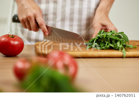 Woman's hands preparing fresh healthy ingredients with a knife on a cutting board, making a salad in the kitchen 140762051