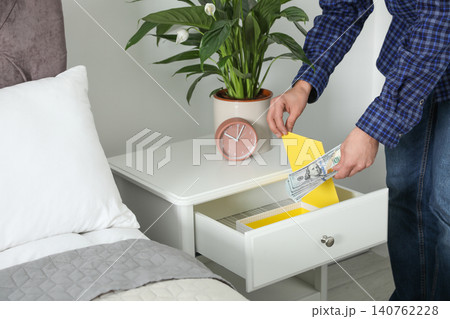 Man hiding dollar banknotes in cabinet indoors, closeup. Money savings Man hiding dollar banknotes in cabinet indoors, closeup. Money savings 140762228