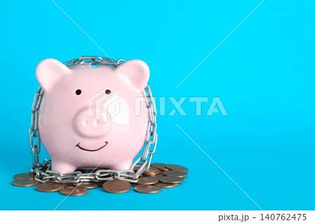 Piggy bank with steel chain and coins on light blue background, space for text. Money safety concept Piggy bank with steel chain and coins on light blue background, space for text. Money safety concept 140762475