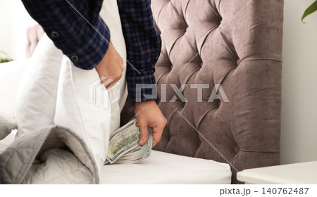 Man hiding dollar banknotes under blanket in bedroom, closeup. Money savings Man hiding dollar banknotes under blanket in bedroom, closeup. Money savings 140762487
