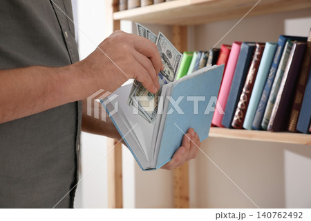 Man hiding money in book indoors, closeup. Financial savings 140762492