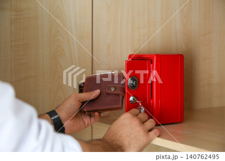 Man putting wallet into small red steel safe, closeup 140762495