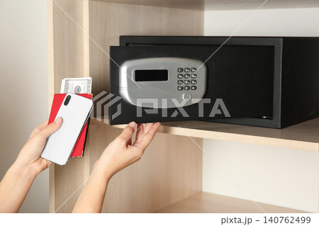 Woman putting smartphone, passport and money into steel safe, closeup Woman putting smartphone, passport and money into steel safe, closeup 140762499