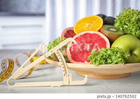 Body fat caliper, measuring tape, vegetables and fruits on table. Diet plan from nutritionist Body fat caliper, measuring tape, vegetables and fruits on table. Diet plan from nutritionist 140762502