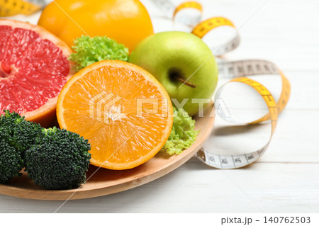 Fruits, vegetables and measuring tape on white wooden background, closeup. Visiting nutritionist Fruits, vegetables and measuring tape on white wooden background, closeup. Visiting nutritionist 140762503