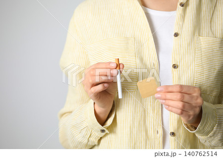Young woman with nicotine patch and cigarette on light grey background, closeup Young woman with nicotine patch and cigarette on light grey background, closeup 140762514