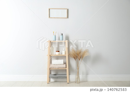 Wooden shelving unit with toiletries near white wall indoors. Bathroom interior element Wooden shelving unit with toiletries near white wall indoors. Bathroom interior element 140762583