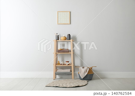 Wooden shelving unit with toiletries near white wall indoors. Bathroom interior element 140762584