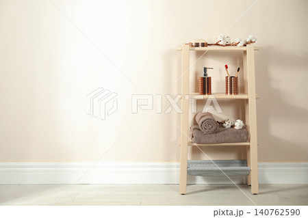 Wooden shelving unit with toiletries near beige wall indoors, space for text. Bathroom interior element 140762590
