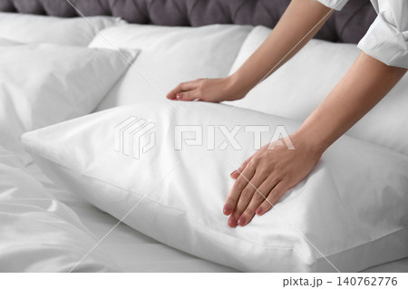Woman fluffing soft pillow in bedroom, closeup 140762776