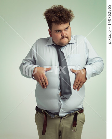 Man, stomach and plus size with belly from unhealthy diet or weight gain on a studio background. Young male person or big guy holding tummy for eating disorder or body conscious on mockup space 140762965