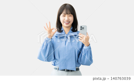 スマートフォンを持ってOKポーズをする若い女性・ビジネスウーマン 140763039