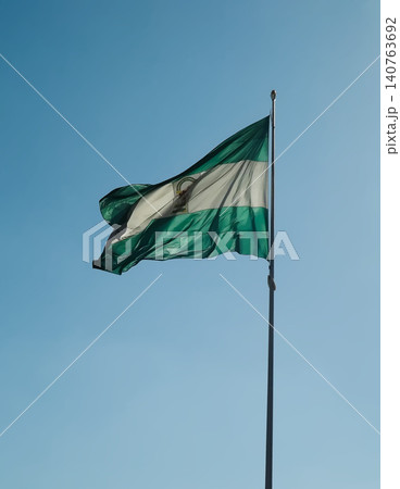 Green and white Andalusian flag waving on the wind against a blue sky. Green and white Andalusian flag waving on the wind against a blue sky. 140763692