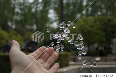 Drips of water floating in the air next to a hand in a park Drips of water floating in the air next to a hand in a park 140764212