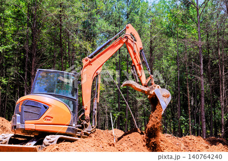 Excavator is working in forested area, moving dirt during digging trenches construction project 140764240