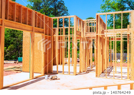 Construction continues with wooden beams frames wall being built in an outdoor setting with unfinished house 140764249