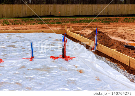 Construction workers prepare ground with tarp pipes for new home slab foundation in residential area. 140764275