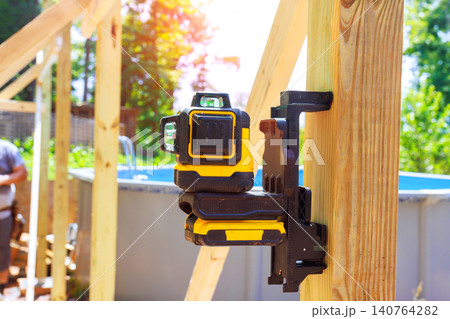 Laser level tool is mounted on wood at construction site where workers are framing building outdoors. 140764282