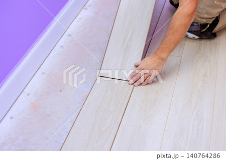 Handy man places wooden floor planks carefully onto foundation in room with purple walls while renovating. Handy man places wooden floor planks carefully onto foundation in room with purple walls while renovating. 140764286