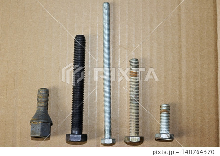 Collection of metal bolts with various lengths, diameters, and threads arranged neatly on a cardboard surface, highlighting construction hardware diversity and industrial fasteners for repair projects 140764370