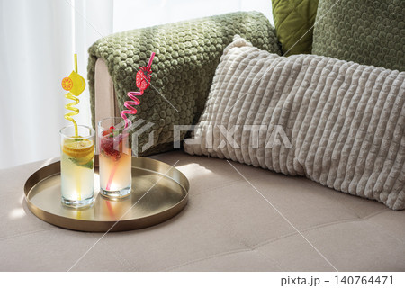 Refreshing summer drinks on tray near cozy sofa cushions 140764471