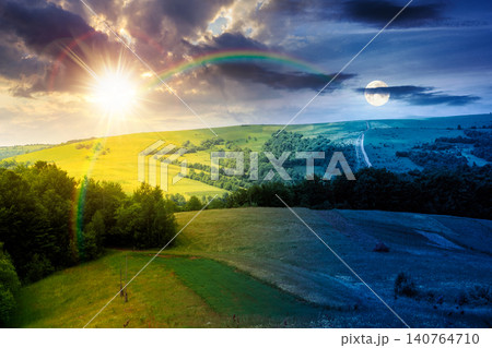 rural fields near mountain in summertime. day meet night. beautiful view of agricultural area. sun and moon in harmony over gorgeous mountain ridge with haystack on a grassy pasture. summer solstice rural fields near mountain in summertime. day meet night. beautiful view of agricultural area. sun and moon in harmony over gorgeous mountain ridge with haystack on a grassy pasture. summer solstice 140764710