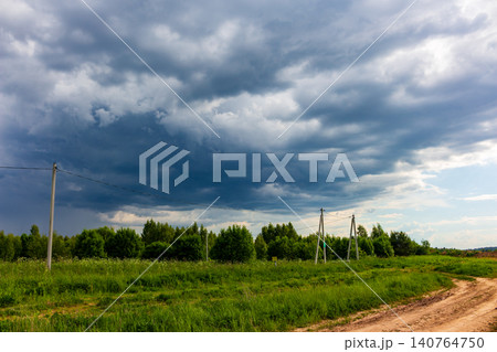 Massive dark storm clouds loom over a lush green meadow and rural dirt road, creating a dramatic and moody atmosphere before the heavy rain begins in the countryside Massive dark storm clouds loom over a lush green meadow and rural dirt road, creating a dramatic and moody atmosphere before the heavy rain begins in the countryside 140764750