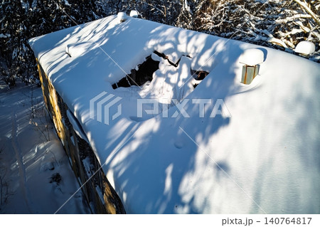 Drone view captures a forgotten winter shack, its broken roof buried in fresh snow. Stark shadows stretch across the icy surface, hinting at cold desolation 140764817
