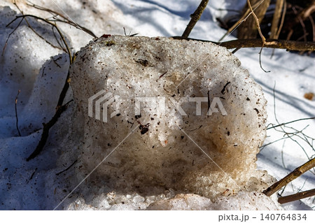 Sun-drenched dirty snow hunk melts, revealing gritty texture and embedded twigs. A symbol of spring's arrival, winter's slow surrender 140764834