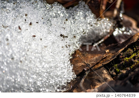 Sparkling spring snow melt shimmers brightly, revealing brown leaves underneath. Glistening icy crystals signal nature's gentle awakening under the warm sun Sparkling spring snow melt shimmers brightly, revealing brown leaves underneath. Glistening icy crystals signal nature's gentle awakening under the warm sun 140764839