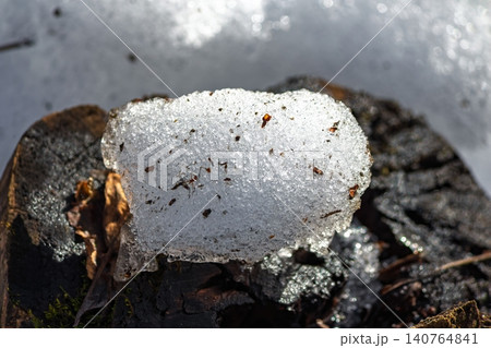 Glistening granular snow melting on a dark stump, revealing intricate ice textures. Early spring thaw, natural detail under bright sun Glistening granular snow melting on a dark stump, revealing intricate ice textures. Early spring thaw, natural detail under bright sun 140764841