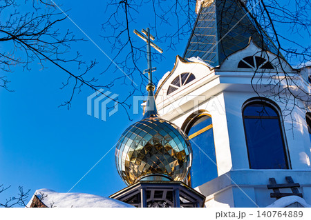 Gleaming gold Orthodox church dome under bright winter sky, construction site partially visible, stark blue background Gleaming gold Orthodox church dome under bright winter sky, construction site partially visible, stark blue background 140764889